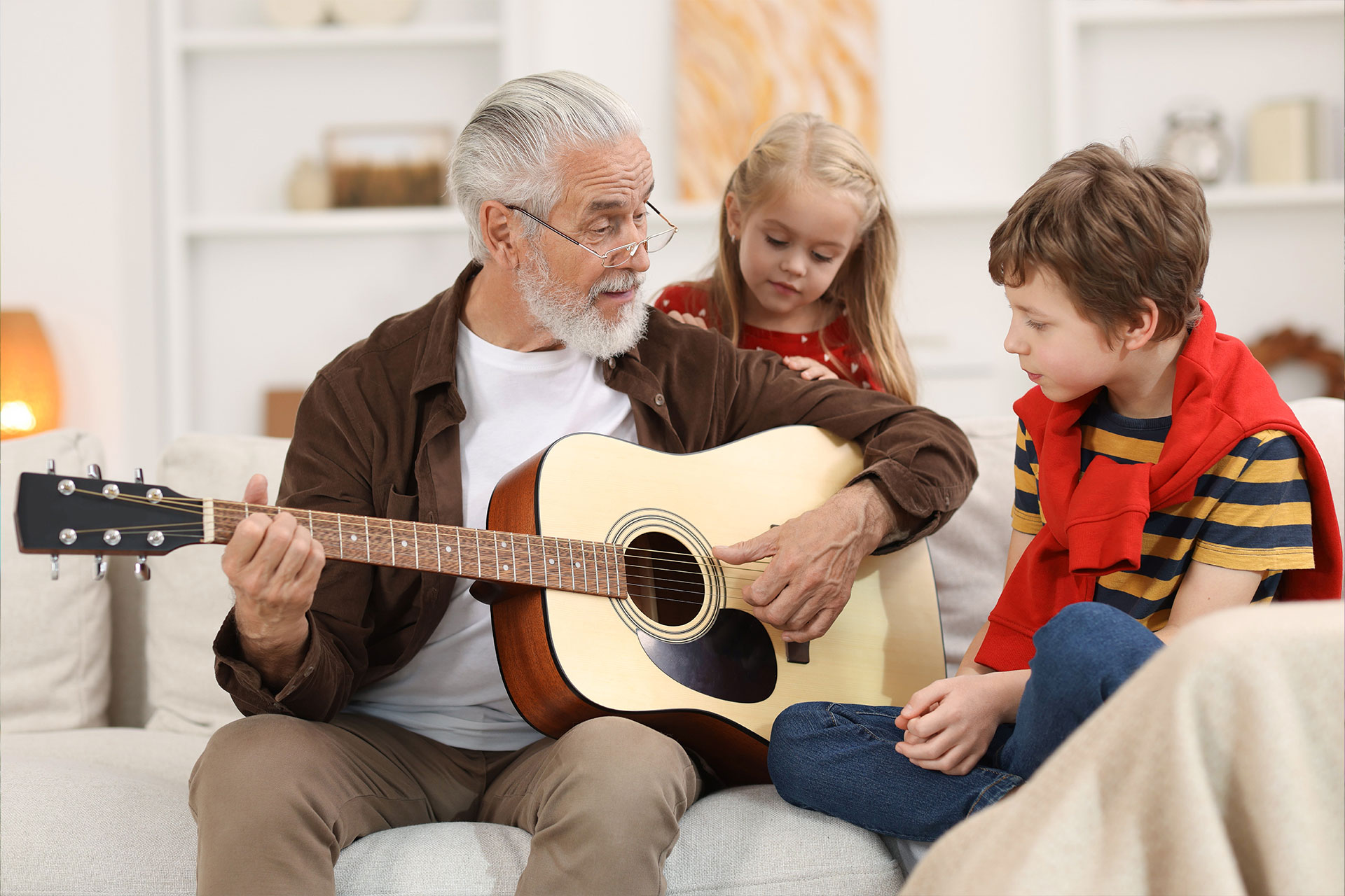 Un nonno suona la chitarra con i due nipoti seduti accanto